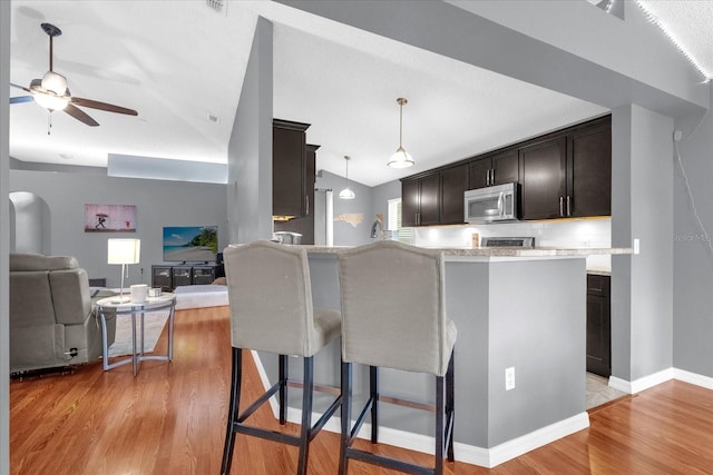 kitchen featuring a breakfast bar, decorative light fixtures, light wood-type flooring, and vaulted ceiling