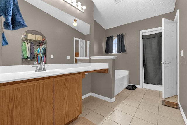 bathroom featuring lofted ceiling, a tub, tile patterned flooring, vanity, and a textured ceiling