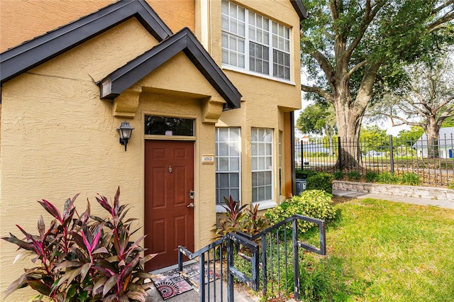 view of exterior entry featuring fence, a lawn, and stucco siding