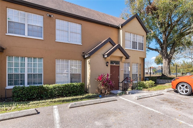 view of front of home with uncovered parking, fence, and stucco siding