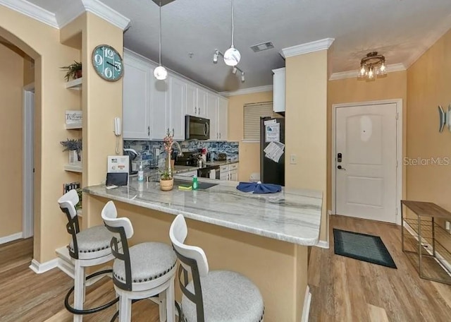 kitchen with hanging light fixtures, kitchen peninsula, white cabinets, appliances with stainless steel finishes, and tasteful backsplash