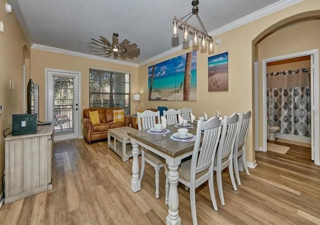 dining area with arched walkways, ceiling fan, ornamental molding, and light wood finished floors