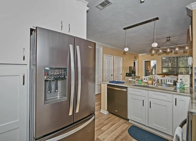 kitchen featuring visible vents, a sink, a peninsula, stainless steel appliances, and white cabinetry