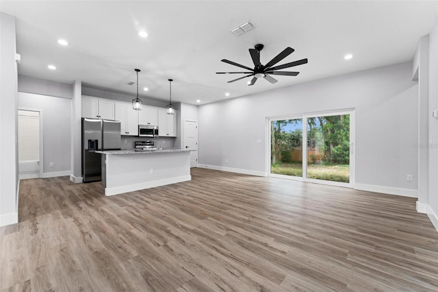 kitchen with stainless steel appliances, a center island with sink, light stone countertops, light wood-type flooring, and white cabinetry