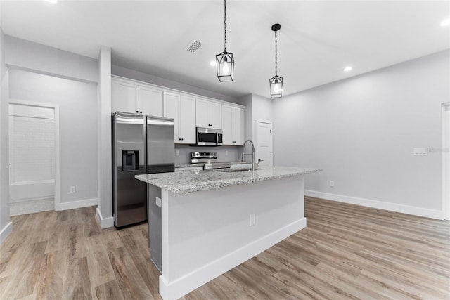 kitchen with light stone countertops, light wood-type flooring, stainless steel appliances, white cabinets, and a kitchen island with sink