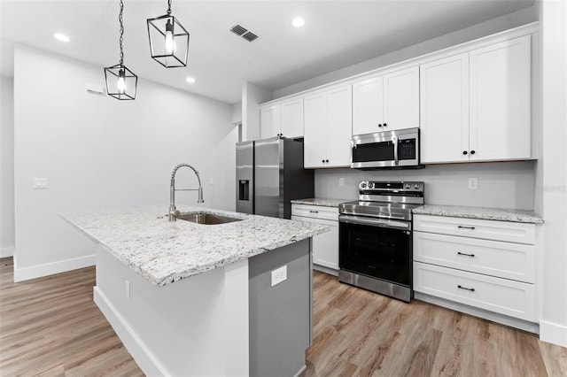 kitchen with a center island with sink, sink, decorative light fixtures, white cabinetry, and appliances with stainless steel finishes