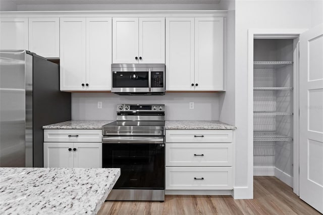 kitchen with white cabinetry, light stone countertops, stainless steel appliances, and light wood-type flooring