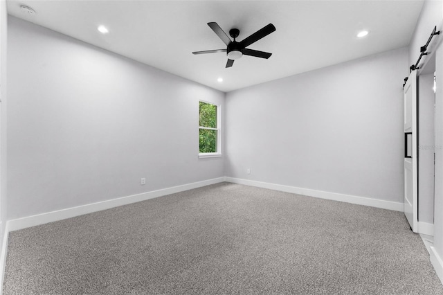 carpeted empty room with ceiling fan and a barn door