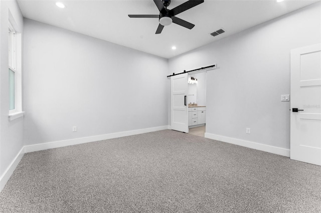 unfurnished bedroom with connected bathroom, ceiling fan, light carpet, and a barn door