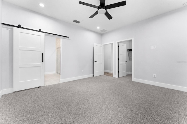 unfurnished bedroom with ensuite bathroom, a barn door, a spacious closet, ceiling fan, and light carpet