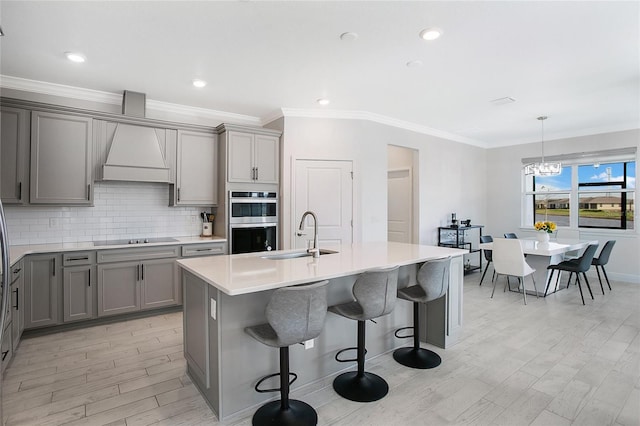 kitchen featuring light hardwood / wood-style flooring, double oven, sink, and a kitchen island with sink