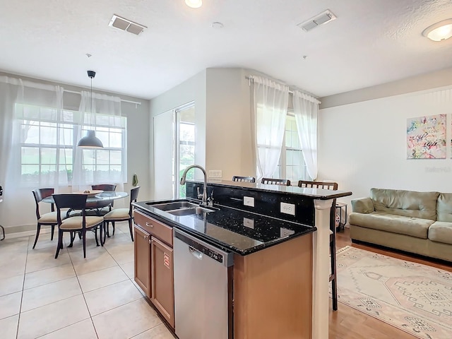 kitchen featuring an island with sink, dishwasher, dark stone countertops, decorative light fixtures, and sink