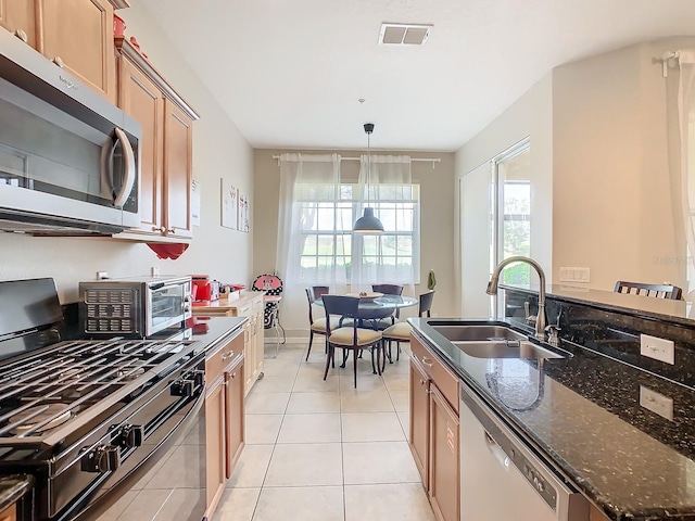 kitchen with appliances with stainless steel finishes, sink, pendant lighting, dark stone countertops, and light tile patterned floors