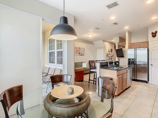 kitchen with a center island with sink, light tile patterned floors, appliances with stainless steel finishes, sink, and decorative light fixtures