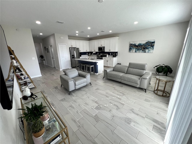 living room featuring sink, a textured ceiling, and light hardwood / wood-style flooring