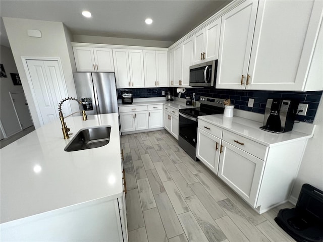 kitchen with backsplash, white cabinetry, light hardwood / wood-style flooring, sink, and stainless steel appliances