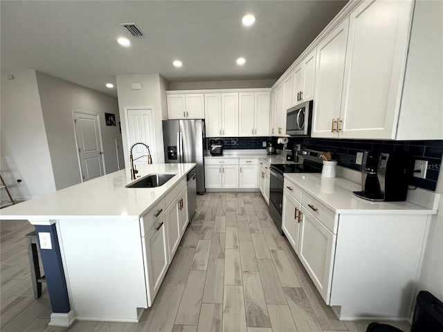 kitchen featuring backsplash, a center island with sink, sink, white cabinets, and appliances with stainless steel finishes