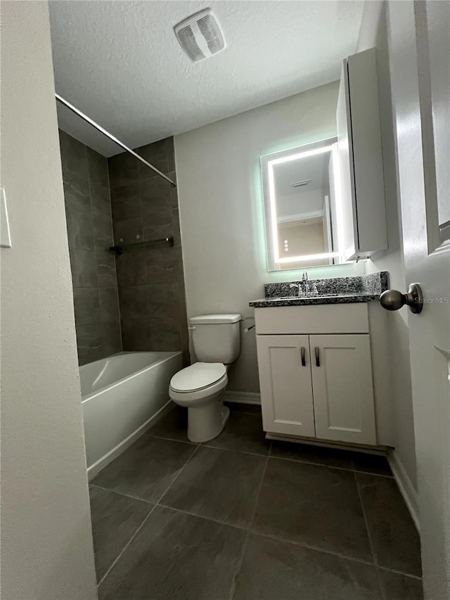 full bathroom featuring toilet, tile patterned flooring, tiled shower / bath combo, vanity, and a textured ceiling