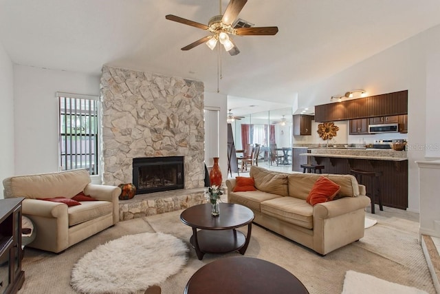 carpeted living room featuring ceiling fan, a stone fireplace, and vaulted ceiling