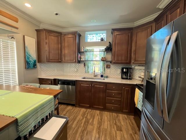 kitchen with decorative backsplash, light hardwood / wood-style flooring, ornamental molding, sink, and appliances with stainless steel finishes