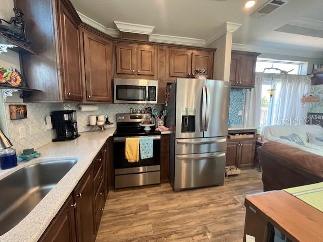 kitchen featuring decorative backsplash, light hardwood / wood-style flooring, ornamental molding, sink, and appliances with stainless steel finishes