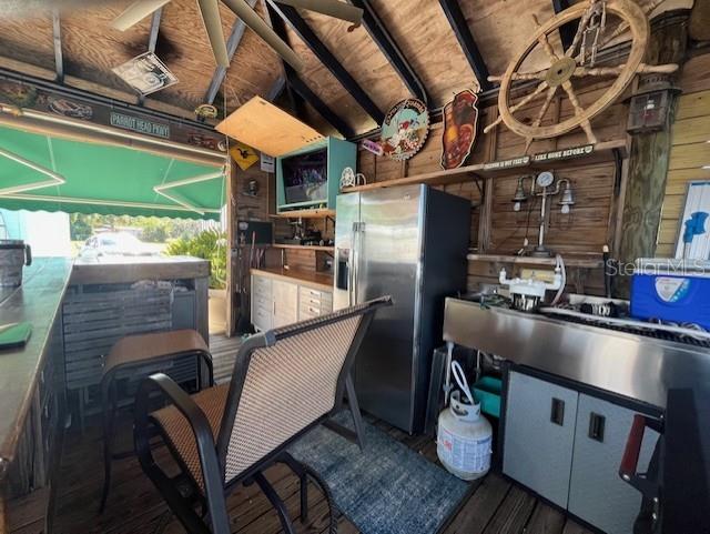 kitchen featuring dark hardwood / wood-style flooring, vaulted ceiling, stainless steel fridge with ice dispenser, and wooden walls