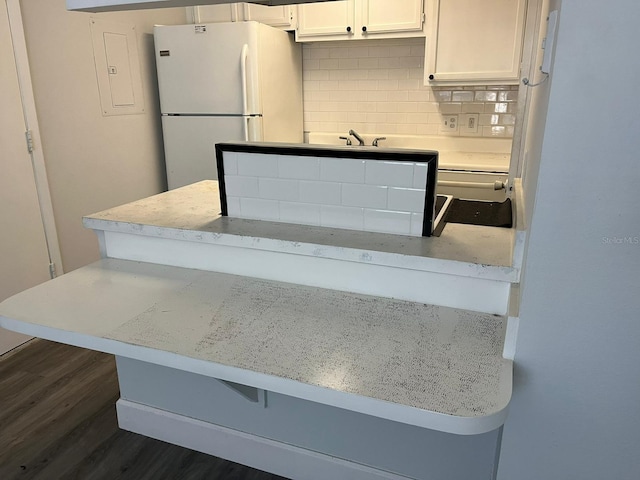 kitchen with white refrigerator, white cabinets, decorative backsplash, a breakfast bar area, and dark wood-type flooring