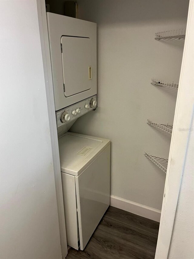 laundry room with dark wood-type flooring and stacked washer / drying machine