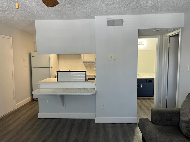 kitchen with decorative backsplash, a textured ceiling, a breakfast bar area, dark hardwood / wood-style floors, and white fridge