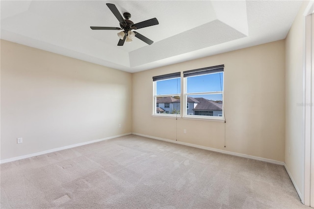 unfurnished room with ceiling fan, light colored carpet, and a raised ceiling