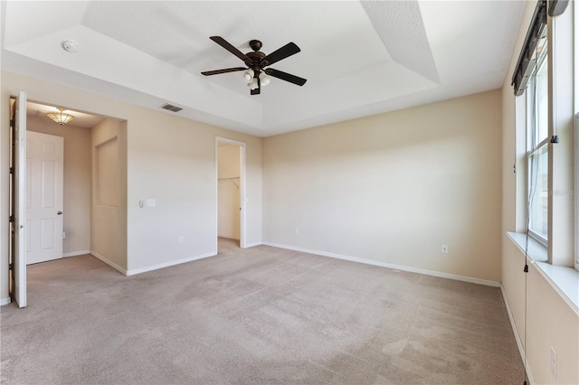 empty room featuring ceiling fan, light carpet, and a raised ceiling