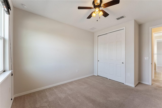 unfurnished bedroom featuring light carpet, multiple windows, a closet, and ceiling fan