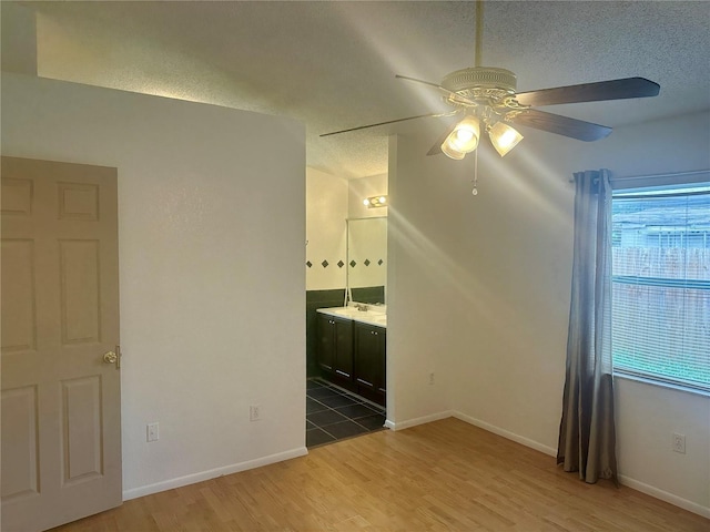 unfurnished bedroom featuring ensuite bathroom, hardwood / wood-style flooring, a textured ceiling, and ceiling fan