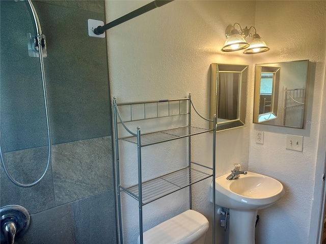 bathroom with sink, a tile shower, and toilet