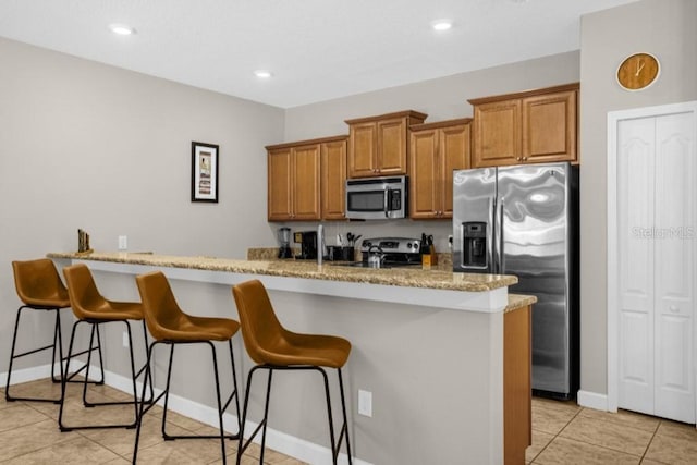 kitchen featuring appliances with stainless steel finishes, light tile patterned flooring, a kitchen bar, kitchen peninsula, and light stone counters