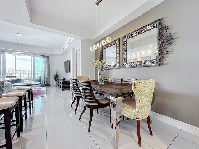 dining area with light tile patterned flooring, a tray ceiling, and baseboards