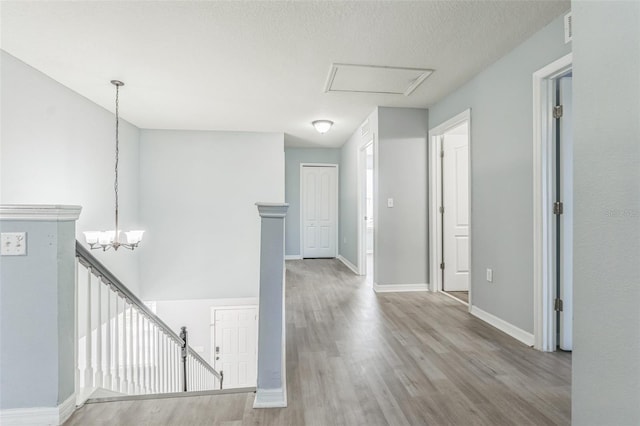 hall with light wood-style floors, baseboards, a notable chandelier, and an upstairs landing