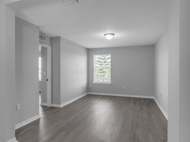 unfurnished room featuring dark wood-type flooring, visible vents, and baseboards