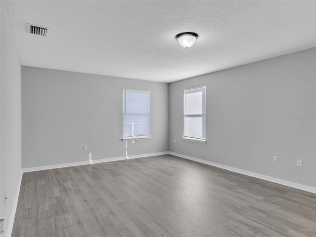 spare room featuring wood finished floors, visible vents, and baseboards