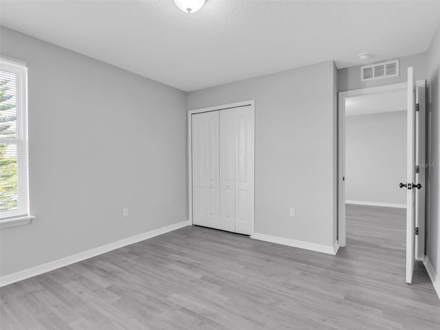 unfurnished bedroom featuring light wood-type flooring, visible vents, baseboards, and multiple windows