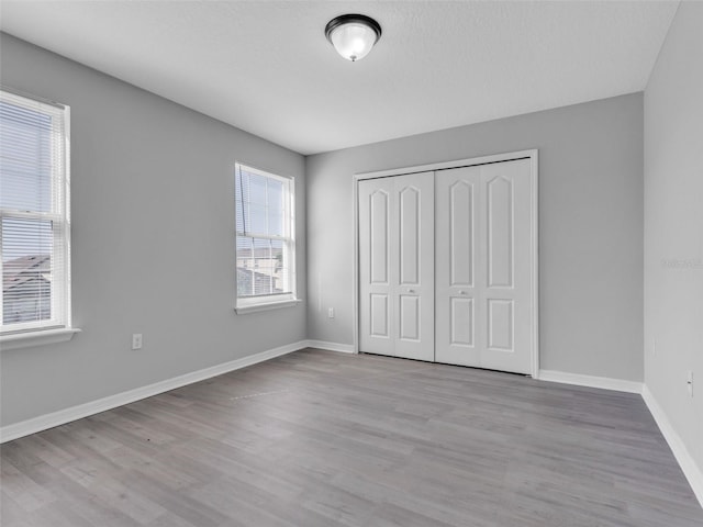 unfurnished bedroom featuring light wood finished floors, baseboards, and a closet