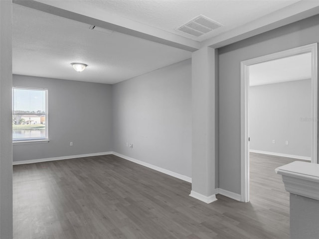 spare room with baseboards, a textured ceiling, visible vents, and dark wood-style flooring