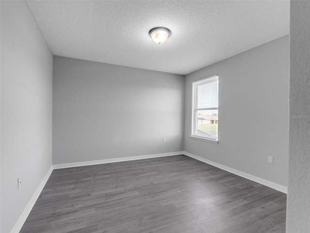 spare room featuring baseboards, dark wood finished floors, and a textured ceiling