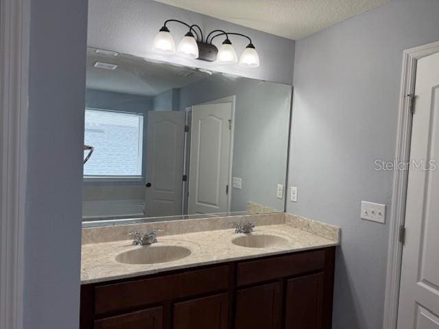 full bath with a textured ceiling, double vanity, a sink, and visible vents