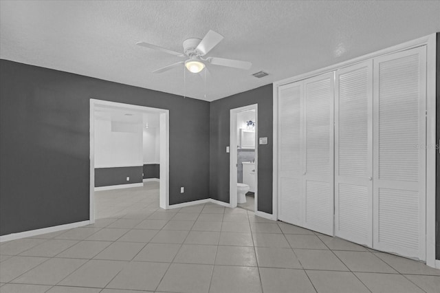 unfurnished bedroom featuring ensuite bathroom, a textured ceiling, ceiling fan, a closet, and light tile patterned flooring