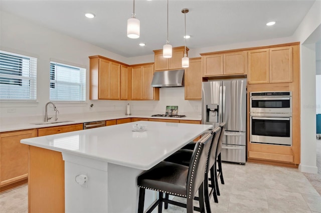 kitchen featuring a center island, under cabinet range hood, light brown cabinetry, appliances with stainless steel finishes, and a sink