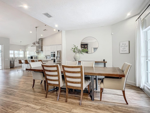 dining area featuring a textured ceiling, light hardwood / wood-style flooring, and vaulted ceiling