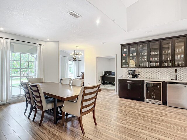 dining space featuring wine cooler, a chandelier, a textured ceiling, and light hardwood / wood-style flooring