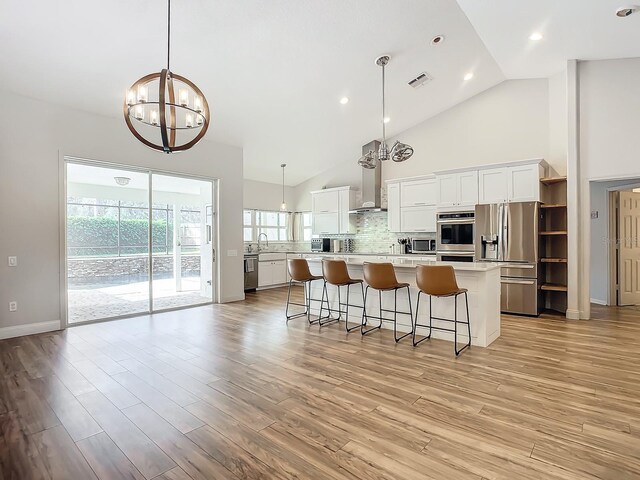 kitchen with white cabinetry, stainless steel appliances, hanging light fixtures, and light hardwood / wood-style flooring