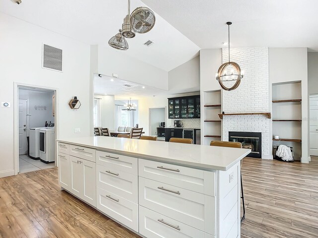 kitchen with a breakfast bar, light hardwood / wood-style flooring, white cabinets, washer and dryer, and vaulted ceiling